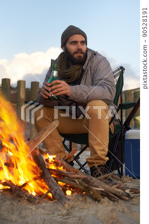 WArming up after a long day. Two young men sitting around a fire on the beach. 90528191