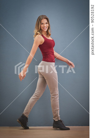 These boots were made for walking. Portrait of a smiling young woman walking in front of a gray wall. These boots were made for walking. Portrait of a smiling young woman walking in front of a gray wall. 90528192