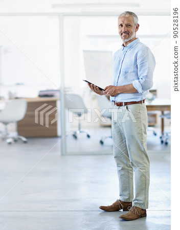 Taking care of business. Full length portrait of a mature businessman using a tablet in his office. Taking care of business. Full length portrait of a mature businessman using a tablet in his office. 90528196
