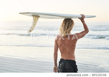 He's riding the waves today. Rearview shot of a young surfer carrying his surfboard over his head at the beach. He's riding the waves today. Rearview shot of a young surfer carrying his surfboard over his head at the beach. 90528336