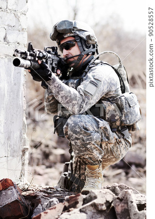 Leading the assult. A soldier crouched down next to a broken down wall and pointing his gun into the distance. Leading the assult. A soldier crouched down next to a broken down wall and pointing his gun into the distance. 90528557