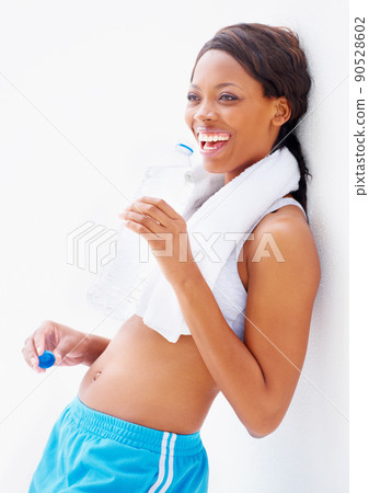 Feeling great after her workout. Smiling young african in gymwear with a towel around her neck while drinking some water. 90528602