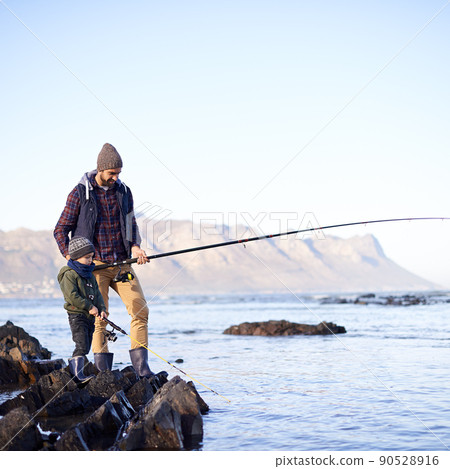 Looks like you got something. Shot of a cute little boy fishing with his father by the sea. 90528916