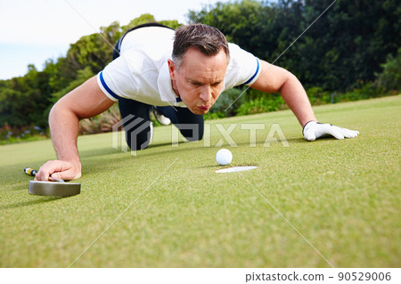 Its not cheating if nobody saw it. Shot of a handsome man trying to blow his golf ball into the hole. 90529006