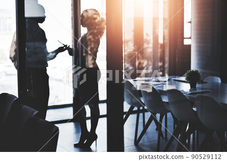 Enhancing business together. Silhouetted shot of two businesspeople having a discussion in an office. Enhancing business together. Silhouetted shot of two businesspeople having a discussion in an office. 90529112