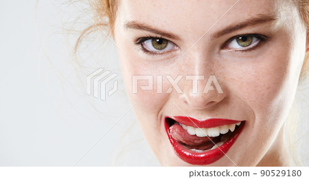 Shes sizzling hot. Closeup studio portrait of a beautiful young woman wearing red lipstick biting her tongue. Shes sizzling hot. Closeup studio portrait of a beautiful young woman wearing red lipstick biting her tongue. 90529180