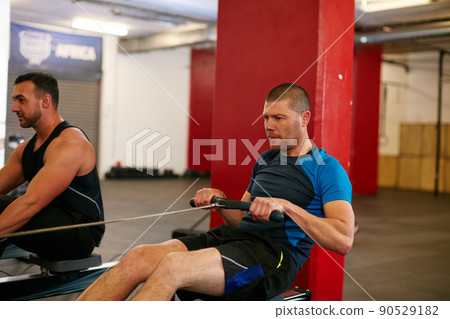 Rowing to get ripped. Cropped shot of two men working out on the rowing machine at the gym. Rowing to get ripped. Cropped shot of two men working out on the rowing machine at the gym. 90529182
