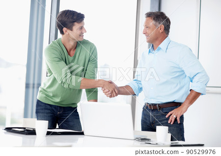 We make a good team. A mature executive shaking the hand of his younger colleague. We make a good team. A mature executive shaking the hand of his younger colleague. 90529976