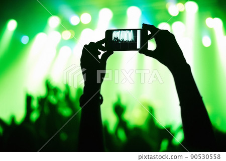 A person filming their favorite band with a camera phone. This concert was created for the sole purpose of this photo shoot, featuring 300 models and 3 live bands. All people in this shoot are model 90530558