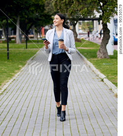 Walking through the caffeine. Shot of a young businesswoman making her way to work while using her smartphone and drinking coffee. Walking through the caffeine. Shot of a young businesswoman making her way to work while using her smartphone and drinking coffee. 90530579
