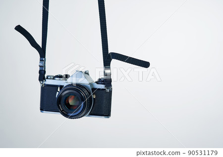 Film photography makes a comeback. Studio shot of a camera hanging by its strap. Film photography makes a comeback. Studio shot of a camera hanging by its strap. 90531179