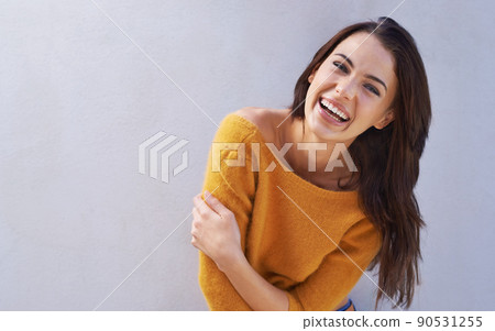 Laughs are fun. Portrait of a beautiful young woman laughing while standing against a gray wall. 90531255