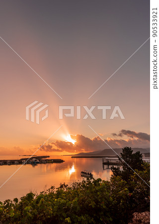Amazing sunrise in the seaside harbor, sunbeams spreading in the sky, boats in the smooth sea. 90533921