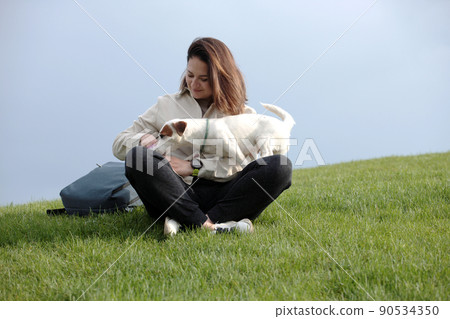 Girl gives tasty patches of dog treats to a white dog on the background of the sky 90534350