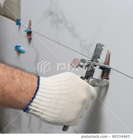 the master holds a tool in his hand, controls the gap between ceramic tiles, laying tiles in the shower room 90534465