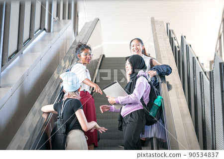 Group of young female students laughing while going up the escalator. Group of young female students laughing while going up the escalator. 90534837