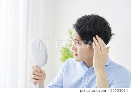 A man looking in the mirror at home and checking his hair 90535014