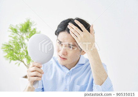 A man looking in the mirror and checking his hair in the living room 90535015