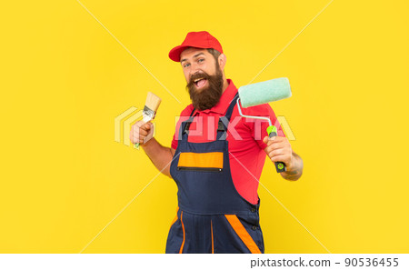 happy man in work clothes hold paint roller and brush on yellow background 90536455