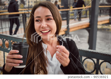 Smiling young woman drinks coffee outside Smiling young woman drinks coffee outside 90536921