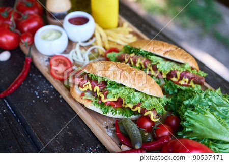 BBQ hot dog served with vegetables and French fries and sauces on wooden serving board 90537471