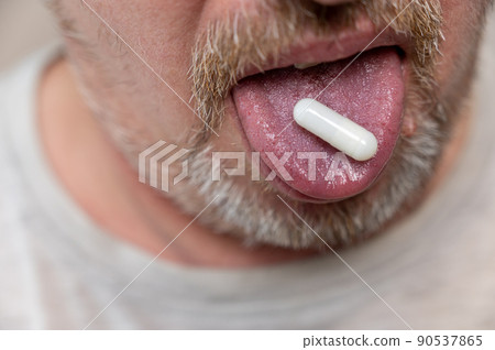 A man takes medication. The lower part of the man's face. The white pill is on his tongue. Mature man with stubble. Gray hair on his beard and mustache. Close-up. Selective focus. A man takes medication. The lower part of the man's face. The white pill is on his tongue. Mature man with stubble. Gray hair on his beard and mustache. Close-up. Selective focus. 90537865