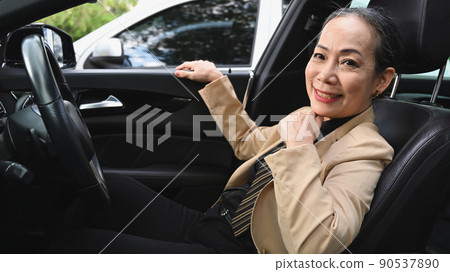 Mature woman in business suit sitting behind the wheel of a car and smiling at camera 90537890