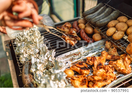 Close-up of man grilling lots of meat on barbecue with flames 90537991