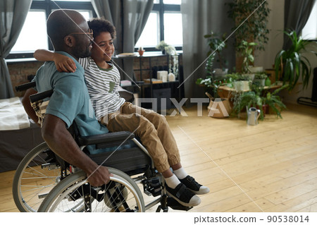 African disabled father riding his son on wheelchair while he sitting on his knees, they playing in the room African disabled father riding his son on wheelchair while he sitting on his knees, they playing in the room 90538014