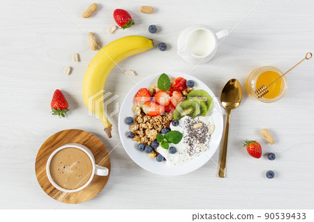 Bowl of granola with yogurt, fresh berries and fruits, cup of coffee on white wooden table background top view. 90539433