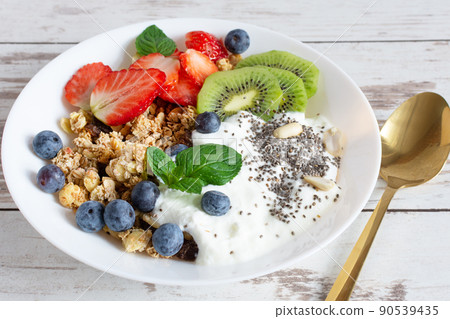 White ceramic bowl of homemade granola with yogurt, fresh berries and fruits on white wooden table background. White ceramic bowl of homemade granola with yogurt, fresh berries and fruits on white wooden table background. 90539435