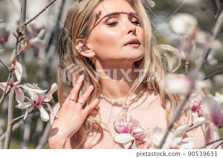Portrait of a beautiful happy middle aged woman enjoying the smell in a blooming spring garden. Beautiful magnolia bushes, large flowers. Portrait of a beautiful happy middle aged woman enjoying the smell in a blooming spring garden. Beautiful magnolia bushes, large flowers. 90539631