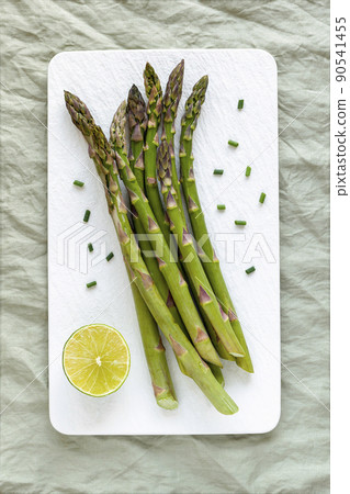 Asparagus stems on the white plate served with green lemon and cut chives 90541455