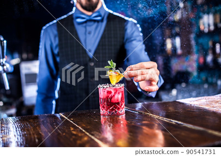 Focused barkeeper adds ingredients to a cocktail at the bar counter 90541731