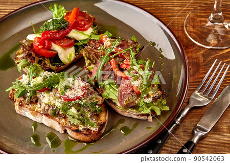 Italian sandwiches - bruschetta with meat pate, arugula, sun dried tomato and seeds on bread on dark wooden table. Italian sandwiches - bruschetta with meat pate, arugula, sun dried tomato and seeds on bread on dark wooden table. 90542063