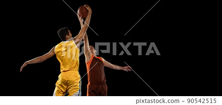 Portrait of two young men, professional basketball players in motion, training isolated over black studio background. Cathcing ball in a jump Portrait of two young men, professional basketball players in motion, training isolated over black studio background. Cathcing ball in a jump 90542515