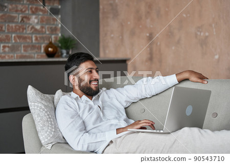 young man using a laptop lying on the couch . young man using a laptop lying on the couch . 90543710