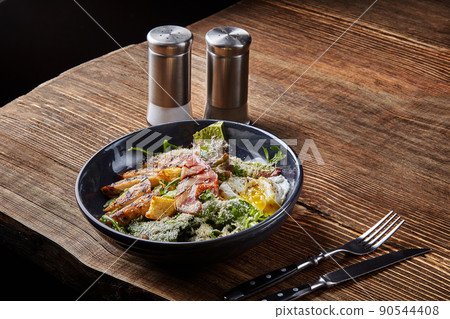 Caesar salad. Caesar dressing is sour taste of vinegar. Often served with Green Cos, topped with Parmesan cheese Costa biscuits, bacon and egg. Dark plate on wooden background Caesar salad. Caesar dressing is sour taste of vinegar. Often served with Green Cos, topped with Parmesan cheese Costa biscuits, bacon and egg. Dark plate on wooden background 90544408