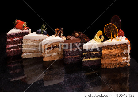 Assorted large pieces of different cakes: chocolate, raspberries, strawberries, nuts, blueberries. Pieces of cakes on a black table. 90545455