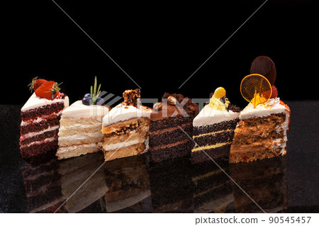 Assorted large pieces of different cakes: chocolate, raspberries, strawberries, nuts, blueberries. Pieces of cakes on a black table. Assorted large pieces of different cakes: chocolate, raspberries, strawberries, nuts, blueberries. Pieces of cakes on a black table. 90545457