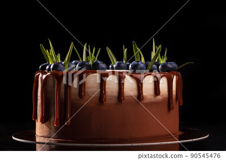 Chocolate cake with blueberries on a black background, decorated with small green leaves and fresh berries 90545476