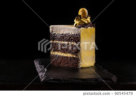Piece of yellow birthday cake. Decorative cream decorations on the cake. Black background. 90545479