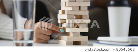 Womans hand pull one of wooden blocks from high build tower 90545508