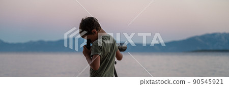 Boy exploring, looking through a telescope standing by the sea 90545921