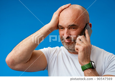 Portrait of an adult man talking on the phone against blue background. 90547569