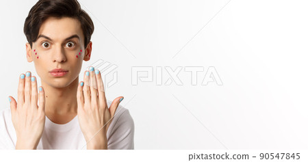 People, lgbtq and beauty concept. Beautiful gay man showing blue nail polish on fingernails and looking at camera, have manicure, standing over white background 90547845