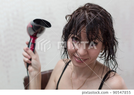 Young woman getting ready for a date, drying her head with a hair dryer in front of a mirror Young woman getting ready for a date, drying her head with a hair dryer in front of a mirror 90547855
