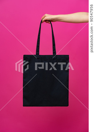 Female hand holding eco or reusable shopping bag against pink background Female hand holding eco or reusable shopping bag against pink background 90547956