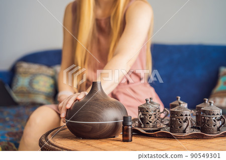 Aromatherapy Concept. Wooden Electric Ultrasonic Essential Oil Aroma Diffuser and Humidifier. Ultrasonic aroma diffuser for home. Woman resting at home Aromatherapy Concept. Wooden Electric Ultrasonic Essential Oil Aroma Diffuser and Humidifier. Ultrasonic aroma diffuser for home. Woman resting at home 90549301