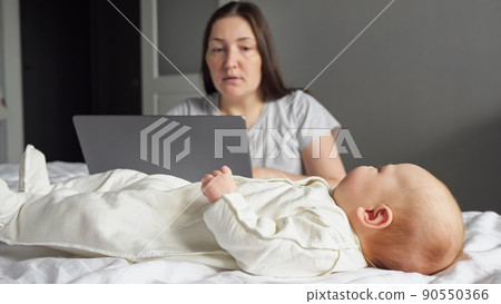 Mother freelancer looks after baby girl working on laptop Mother freelancer looks after baby girl working on laptop 90550366